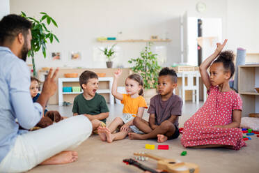 Eine Gruppe von kleinen Kindergartenkindern, die in einem Klassenzimmer auf dem Boden sitzen. - HPIF09011