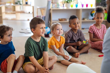 A group of small nursery school children sitting on floor indoors in classroom. - HPIF09013