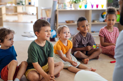 Eine Gruppe von kleinen Kindergartenkindern, die in einem Klassenzimmer auf dem Boden sitzen. - HPIF09013