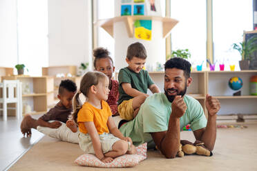 A group of small nursery school children with man teacher sitting on floor indoors in classroom, playing. - HPIF09028