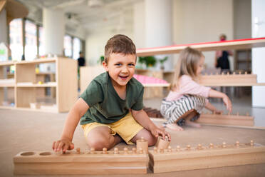 Eine Gruppe von kleinen Kindergartenkindern spielt drinnen im Klassenzimmer, Montessori-Lernen. - HPIF09031