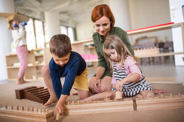 Gruppe von kleinen Kindergartenkindern mit Lehrer auf dem Boden sitzend in einem Klassenzimmer, Montessori-Lernkonzept. - HPIF09032