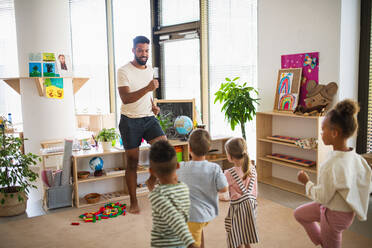 A group of small nursery school children with man teacher standing indoors in classroom, doing exercise. - HPIF09034