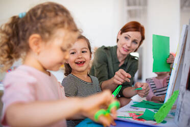 Eine Gruppe von kleinen Kindergartenkindern mit einer Lehrerin in einem Klassenzimmer, Kunst- und Bastelkonzept. - HPIF09042