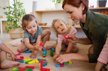 Eine Gruppe von kleinen Kindergartenkindern mit einer Lehrerin auf dem Boden in einem Klassenzimmer, beim Spielen. - HPIF09043