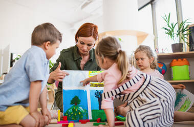 Eine Gruppe von kleinen Kindergartenkindern mit Lehrerin auf dem Boden im Klassenzimmer, beim Lernen. - HPIF09044