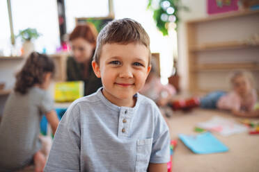 Ein Porträt eines kleinen Kindergartenjungen in einem Klassenzimmer, der in die Kamera schaut. - HPIF09047