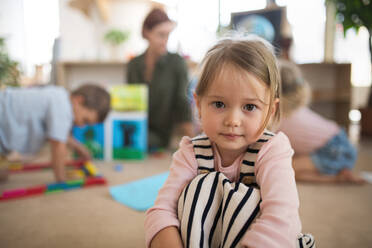 Ein Porträt eines kleinen Kindergartenmädchens in einem Klassenzimmer, das in die Kamera schaut. - HPIF09049