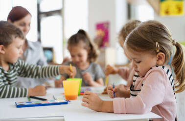 Eine Gruppe kleiner Kindergartenkinder mit einer Lehrerin in einem Klassenzimmer beim Malen. - HPIF09058