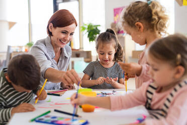 Eine Gruppe kleiner Kindergartenkinder mit einer Lehrerin in einem Klassenzimmer beim Malen. - HPIF09060