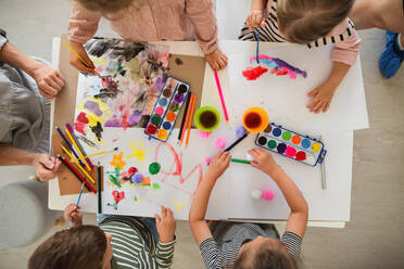 Draufsicht auf eine Gruppe von kleinen Kindergartenkindern mit Lehrerin in einem Klassenzimmer, Malerei. - HPIF09061