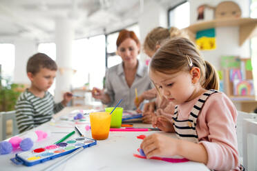 Eine Gruppe kleiner Kindergartenkinder mit einer Lehrerin in einem Klassenzimmer beim Malen. - HPIF09062