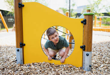 Ein kleiner Kindergartenjunge spielt auf einem Spielplatz im Freien und schaut in die Kamera - HPIF09065