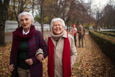 Glückliche ältere Frauen, die im Herbst im Stadtpark spazieren gehen und in die Kamera schauen. - HPIF09075