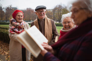 Eine Gruppe glücklicher älterer Freunde mit einem Buch auf einem Herbstspaziergang im Park, die lesen und sich unterhalten. - HPIF09084