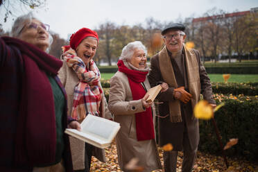 Eine Gruppe glücklicher älterer Freunde mit Büchern auf einem Spaziergang im Park im Herbst, die sich unterhalten und lachen - HPIF09092