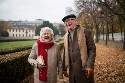 Ein glückliches älteres Paar beim Spaziergang im Park im Herbst, das sich umarmt, lacht und in die Kamera schaut - HPIF09100