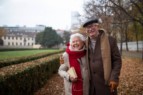 Ein glückliches älteres Paar beim Spaziergang im Park im Herbst, das sich umarmt, lacht und in die Kamera schaut - HPIF09102