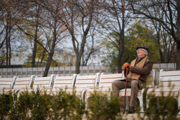 Ein alter eleganter Mann mit Spazierstock sitzt auf einer Bank im Park an einem Herbsttag - HPIF09116