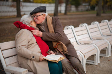 Ein glückliches älteres Paar sitzt auf einer Bank und umarmt sich im Herbst draußen im Stadtpark. - HPIF09123