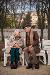 A happy senior friends on sitting on bench and talking outdoors in park on autumn day. - HPIF09124