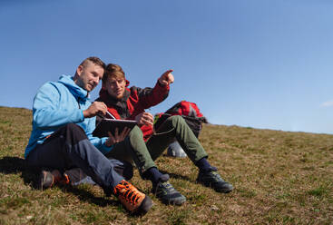 Two paragliders men sitting on the top of the mountain with tablet and looking at view. - HPIF09141