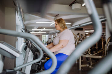 Eine glückliche übergewichtige Frau im mittleren Erwachsenenalter, die in einem Fitnessstudio auf einem Stepper trainiert - HPIF09165
