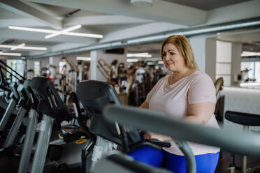 Eine glückliche übergewichtige Frau im mittleren Erwachsenenalter, die in einem Fitnessstudio auf einem Stepper trainiert - HPIF09166