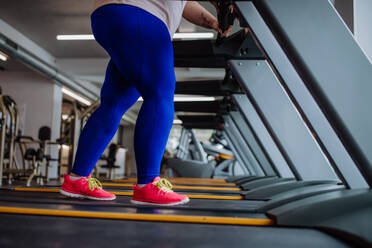 Niedriger Ausschnitt einer übergewichtigen Frau mit Kopfhörern, die in einem Fitnessstudio auf einem Laufband trainiert - HPIF09169