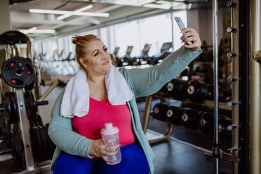 Eine fröhliche Frau in der Lebensmitte macht ein Selfie nach dem Training im Fitnessstudio und bekennt sich zu ihrem positiven Körpergefühl - HPIF09175