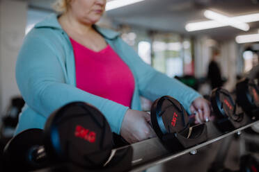 Eine unerkennbare Frau mit Übergröße trainiert mit Hanteln in einem Fitnessstudio - HPIF09177