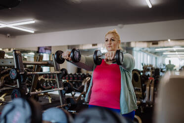 Eine Frau mit Übergröße trainiert und hebt Hanteln drinnen im Fitnessstudio - HPIF09178