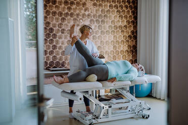 A mid adult physiotherapist woman exercising with overweight woman indoors in rehabilitation center - HPIF09186