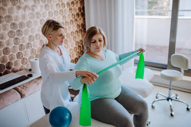 A mid adult physiotherapist woman exercising with overweight woman indoors in rehabilitation center - HPIF09193