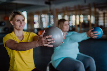 Ein Personal Trainer Training übergewichtige Frau, sitzt auf fintess bal und übt in der Turnhalle. - HPIF09196