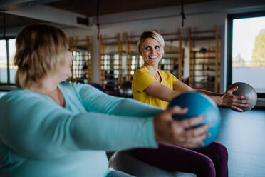 Eine glückliche übergewichtige Frau, die auf einem Fintess-Ball sitzt und mit einem Personal Trainer im Fitnessstudio trainiert - HPIF09198