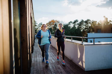 Eine übergewichtige Frau, die mit einem Personal Trainer im Freien auf der Terrasse eines Fitnessstudios trainiert. - HPIF09202