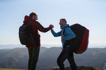 Paragliders high fiving after walking up hill to a paragliding starting point, on a sunny morning in mountains. - HPIF09210