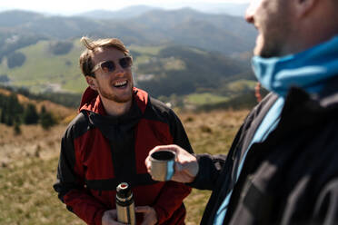 Zwei Gleitschirmflieger stehen auf dem Gipfel eines Berges und trinken einen Tee. - HPIF09215