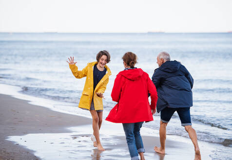 A senior couple and their preteen granddaughter running and having fun on sandy beach. - HPIF09226