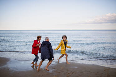 A senior couple and their preteen granddaughter running and having fun on sandy beach. - HPIF09228