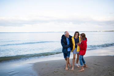 Ein älteres Ehepaar und seine Enkelin im Teenageralter umarmen sich beim Spaziergang am Sandstrand. - HPIF09229