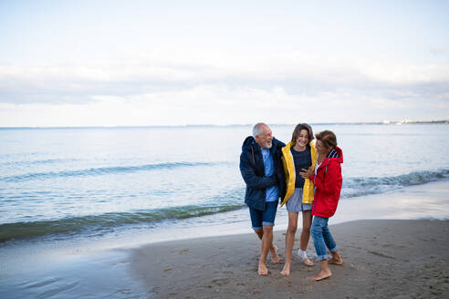 A senior couple and their preteen granddaughter hugging when walking on sandy beach. - HPIF09229