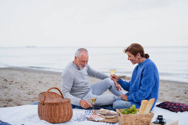 Ein glückliches, verliebtes älteres Paar sitzt auf einer Decke und macht ein Picknick im Freien am Strand am Meer. - HPIF09260