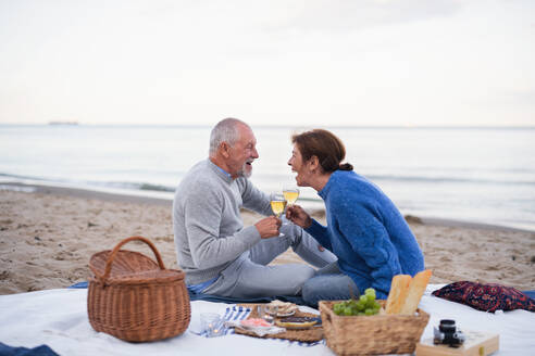 Ein glückliches, verliebtes älteres Paar sitzt auf einer Decke und macht ein Picknick im Freien am Strand am Meer. - HPIF09262