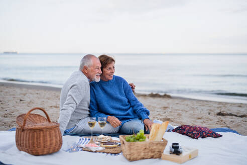 Ein glückliches, verliebtes älteres Paar sitzt auf einer Decke und macht ein Picknick im Freien am Strand am Meer. - HPIF09263