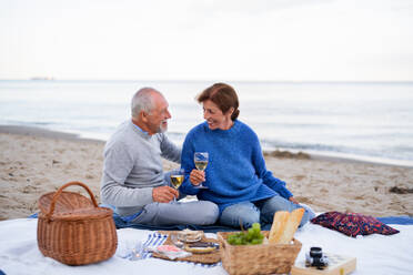 A happy senior couple in love sitting on blanket and embracing when having picnic outdoors on beach - HPIF09265