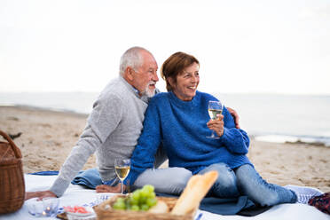 A happy senior couple in love sitting on blanket and embracing when having picnic outdoors on beach - HPIF09266