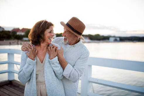 Ein glückliches älteres Paar, das sich im Freien am Pier am Meer umarmt und sich gegenseitig anschaut. - HPIF09279