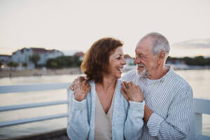 Ein glückliches älteres Paar, das sich im Freien am Pier am Meer umarmt und sich gegenseitig anschaut. - HPIF09280